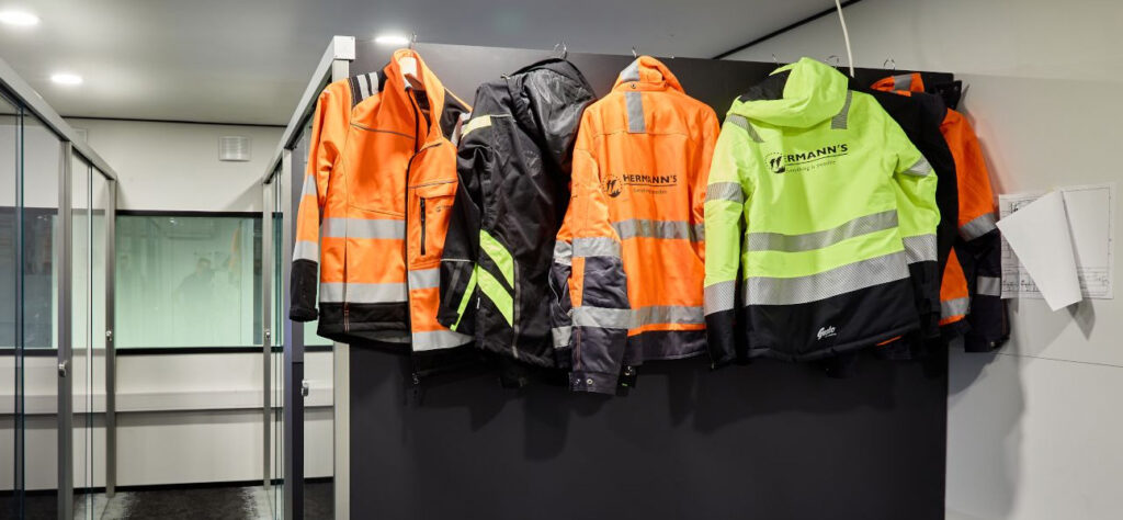 Oransseja ja keltaisia työtakkeja naulakossa, Hermanssin logo selässä